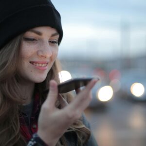 Young woman smiling while using a smartphone on an urban street during twilight.