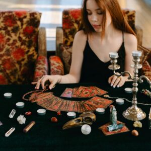 Mystical scene with a woman reading tarot cards surrounded by gemstones and candles.