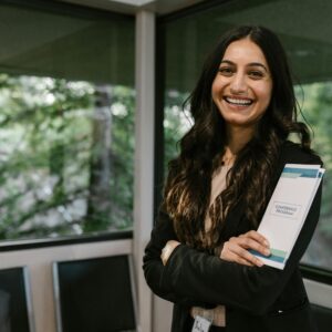 Confident woman holding conference program, smiling in modern indoor setting.